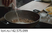 The cook pours cream into a frying pan with champignons on the stove. Стоковое видео, видеограф Strunov David / Фотобанк Лори