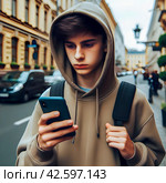 Юноша с капюшоном на голове на улице города мегаполиса залипает в смартфоне. Опасная зависимость от гаджетов и невнимательность. Номофобия - страх остаться без телефона. Стоковое AI-изображение, AI-художник Sergei Gorin / Фотобанк Лори