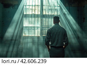 Rear view of a male in gray clothing, facing away from the camera, standing inside a jail cell with light shining through. ,    Generative AI. Стоковое AI-изображение, AI-художник Анна Кривицкая / Фотобанк Лори