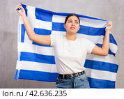 Sad young woman holding Greece flag against unicoloured background. Стоковое фото, фотограф Яков Филимонов / Фотобанк Лори