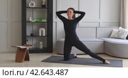 Athletic brunette performs side bends in parighasana, deadbolt pose, practicing yoga at home, training in black sports overalls on the mat, full-length view. Стоковое видео, видеограф Сергей Чайко / Фотобанк Лори