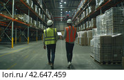 Two engineers, a man and a woman in yellow vests and protective helmets, walk through a large industrial warehouse. Стоковое AI-изображение, AI-художник Ярославский Максим / Фотобанк Лори