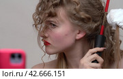 Extreme closeup view of a blondie woman with long hair is using a curling wand to style hair, manually wrapping sections of blonde hair around the wand, making curls (2024 год). Редакционное видео, видеограф А. А. Пирагис / Фотобанк Лори