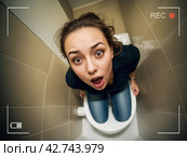 Молодая женщина возмущена, встала на крышку унитаза и заметила скрытую видео камеру, ведущую запись. Стоковое AI-изображение, AI-художник Vladimir Vikhrov / Фотобанк Лори