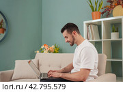 Smiling caucasian young man Working Online On Laptop At Home looking at camera. Стоковое фото, фотограф Raquel Corcoles Mendez / Фотобанк Лори