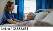 A nurse communicates with a smile with an elderly woman lying on a hospital bed in a hospital room. Стоковое AI-изображение, AI-художник Ярославский Максим / Фотобанк Лори