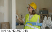 Professional female painter in protective helmet and yellow vest paints the walls with a paint roller. Стоковое видео, видеограф Яков Филимонов / Фотобанк Лори