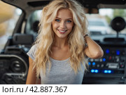 A beautiful blonde girl at an auto sound competition. Car music. Subwoofers, amplifiers, acoustics. Car audio system. Стоковое AI-изображение, AI-художник Александр Поташев / Фотобанк Лори