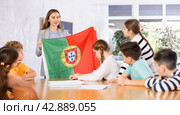 Female teacher, conducting extracurricular lesson in the school class tells schoolchildren the history of Portugal and shows national flag of country. Стоковое фото, фотограф Яков Филимонов / Фотобанк Лори