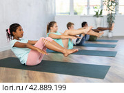 Children doing yoga with group in studio, lying on mat with knee pressed to chest with hands, performing hamstring and low back stretching Ardha Pawanmuktasana. Стоковое фото, фотограф Яков Филимонов / Фотобанк Лори