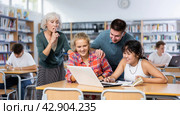 Elderly teacher asks to be quieter than noisy teenagers in school library. Стоковое фото, фотограф Яков Филимонов / Фотобанк Лори