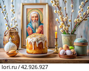 Orthodox Easter. Easter cake, painted eggs, icons, faces of saints, flowers, church candles and Easter decor on a wooden table in an old village house. Стоковое AI-изображение, AI-художник Photojuli / Фотобанк Лори