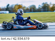 male kart racer drives quickly along the circuit of the autodrome, side view. Стоковое AI-изображение, AI-художник Александр Довянский / Фотобанк Лори