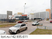 Внутренний двор в новом жилом районе новостройке. Огороженный тротуар, проезжая часть с припаркованными автомобилями, на заднем плане детское образовательное учреждение (школа) за ограждением. Многоэтажные разноцветные жилые дома. (2024 год). Редакционное фото, фотограф Сергей Никифоров-Гордеев / Фотобанк Лори