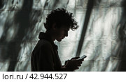 Man gazes at his phone by window, immersed in Entertainment or Music. Стоковое AI-изображение, AI-художник Юрий Поздников / Фотобанк Лори