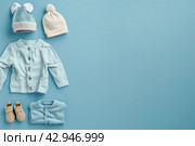 Stack of baby knitted clothes on a table. Set of newborn child rompers, hat and jumper. Fashion infant accessories isolated pastel blue background, empty space. Kid's toys and clothes. Стоковое AI-изображение, AI-художник Марина Демидюк / Фотобанк Лори