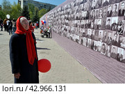 Пожилая женщина в красном платке и шариком в руках стоит возле стены памяти. Город Тюмень (2016 год). Редакционное фото, фотограф Александр Тараканов / Фотобанк Лори
