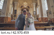 The bride and groom walk and kiss through a Catholic church. Стоковое видео, видеограф Mikhail Davidovich / Фотобанк Лори