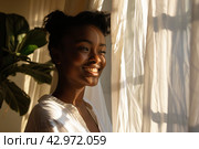 Young african american woman unveil curtain and looking out of window in the morning. Beautiful girl after waking up fully rested and open curtains. Start the new day with happiness. Relax, resting. Стоковое AI-изображение, AI-художник Марина Демидюк / Фотобанк Лори