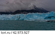 A wall of blue ice rises above a glacial turquoise lake. Thawed ice floes, icebergs floating in the water. Mountains in fog and clouds. Perito Moreno glacier. Lago Argentino. El Calafate. Argentina. Стоковое фото, фотограф Вера Ивановна Кубарева / Фотобанк Лори