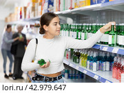 Young female shopper choosing Korean soju bottle at liquor store. Стоковое фото, фотограф Яков Филимонов / Фотобанк Лори