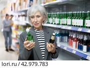 Senior lady choosing bottle of Korean soju at local liquor store. Стоковое фото, фотограф Яков Филимонов / Фотобанк Лори