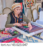 Senior woman weaves rug with Kazakh pattern on handloom at crafts fair, Almaty, Kazakhstan (2024 год). Редакционное фото, фотограф Ирина Кононова / Фотобанк Лори