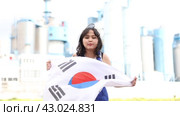 Sad young woman holding big flag of South Korea against background of factory. Стоковое видео, видеограф Яков Филимонов / Фотобанк Лори