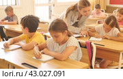 Diligent tweens studying in classroom, listening to lecturer and writing in notebooks. Стоковое видео, видеограф Яков Филимонов / Фотобанк Лори