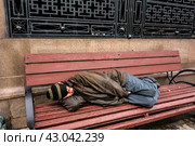 A homeless man sleeps on a bench on the street in the center of Moscow/ Бездомный бомж спит на улице осенью на скамейке в Москве (1916 год) (2016 год). Редакционное фото, фотограф Iva Noel / Фотобанк Лори