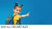 A little girl with a large school backpack on a blue background points her finger at an empty space. Copy space. Стоковое AI-изображение, AI-художник Ярославский Максим / Фотобанк Лори