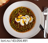 Guisantes a la Murciana - Peas Murcia Style. Juicy peas sauteed with cured ham served with boiled egg on plate, popular Spanish. Стоковое фото, фотограф Яков Филимонов / Фотобанк Лори