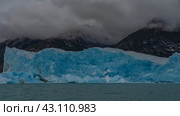 A block of blue ice rises like a wall above a glacial lake. Coastal mountains in clouds and fog. Icebergs float in glacial water. Perito moreno glacier. El Calafate. Argentina. Lago Argentino. Стоковое фото, фотограф Вера Ивановна Кубарева / Фотобанк Лори