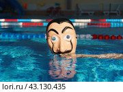 Moscow region, Russia - March 17, 2023: Somebody put on Salvador Dali mask in the swimming pool. Blue water background. Bright sun. Abstraction. Close up conceptual image. Looking at camera. Редакционное фото, фотограф YuryKara / Фотобанк Лори