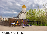 Велосипед и самокаты для аренды стоят на парковке возле храма (2024 год). Редакционное фото, фотограф Юрий Шурчков / Фотобанк Лори