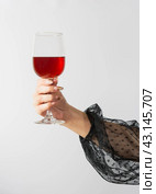 The hand of a girl in an evening black dress holds a glass with red wine. parties, birthday and christmas celebrations. Стоковое фото, фотограф Дмитрий Львович Алферов / Фотобанк Лори