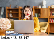 Unhappy frowning asian woman forgetting smth working on laptop. Стоковое фото, фотограф Natalia Gdovskaia / Фотобанк Лори