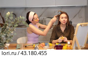 Two close female friends enjoying joint moment of beauty routine at home, with one applying hair rollers to other hair at table in front to vanity mirror. Стоковое видео, видеограф Яков Филимонов / Фотобанк Лори