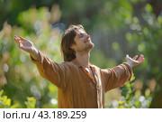 Young man stands with her arms outstretched to the side in the evening park at sunset. To embrace nature. Feeling free outdoor. Winning life achievement, freedom and successful business goal concept. Стоковое AI-изображение, AI-художник Марина Демидюк / Фотобанк Лори