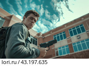 Young man walking with a gun on the background of the school, school shootings concept, school violence. Стоковое AI-изображение, AI-художник Anastacia Gaikova / Фотобанк Лори