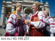 Девушки в русских национальных костюмах водят хороводы и поют народные песни у арки Центрального входа на территорию выставочного комплекса ВДНХ в городе Москве, Россия (2024 год). Редакционное фото, фотограф Николай Винокуров / Фотобанк Лори