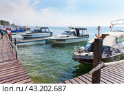 LISTVYANKA VILLAGE, IRKUTSK REGION, RUSSIA - August 03, 2023: Embankment in the village of Listvyanka and a wooden pier for pleasure boats on the shore of Lake Baikal on a summer day. Редакционное фото, фотограф Виктория Катьянова / Фотобанк Лори