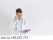 Young trainee doctor intern stands on white background. Handsome red- haired man, thinking. Стоковое фото, фотограф Natalia Gdovskaia / Фотобанк Лори