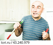 Imposing man iholds in teeth of screws and holding hammer. Стоковое фото, фотограф Татьяна Яцевич / Фотобанк Лори