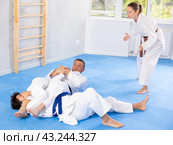 Judo or jiu-jitsu classes - two men practicing grabbing and throwing on sports mats under the guidance of trainer. Стоковое фото, фотограф Яков Филимонов / Фотобанк Лори