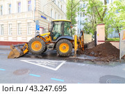 Трактор ведет ремонтные работы на улице города. Работы по прокладке коммуникаций. Экскаватор с ковшом и отвалом копает траншею (2024 год). Редакционное фото, фотограф Константин Григорьев / Фотобанк Лори