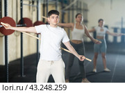 Young guy, together with other athletes, does a warm-up using a long stick in gym. Стоковое фото, фотограф Яков Филимонов / Фотобанк Лори