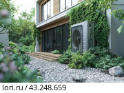 Modern private residence with large window and wooden terrace. An air conditioning system or heat pump is installed on the wall of the building. The facade of the building is decorated with green climbing plants, which create a harmonious and environmentally friendly appearance. In the foreground is a well-kept garden with ornamental plants and a gravel path that leads to the terrace. The stage is surrounded by greenery, which creates a feeling of comfort and closeness to nature. Стоковое AI-изображение, AI-художник Анна Кривицкая / Фотобанк Лори