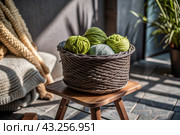 Balls of yarn in a wicker basket on a wooden stool. Needlework, textiles, knitting. Winter season, small business, handmade clothes. Стоковое AI-изображение, AI-художник Photojuli / Фотобанк Лори