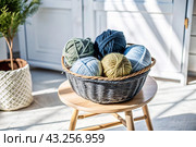 Balls of yarn in a wicker basket on a wooden stool. Needlework, textiles, knitting. Winter season, small business, handmade clothes. Стоковое AI-изображение, AI-художник Photojuli / Фотобанк Лори